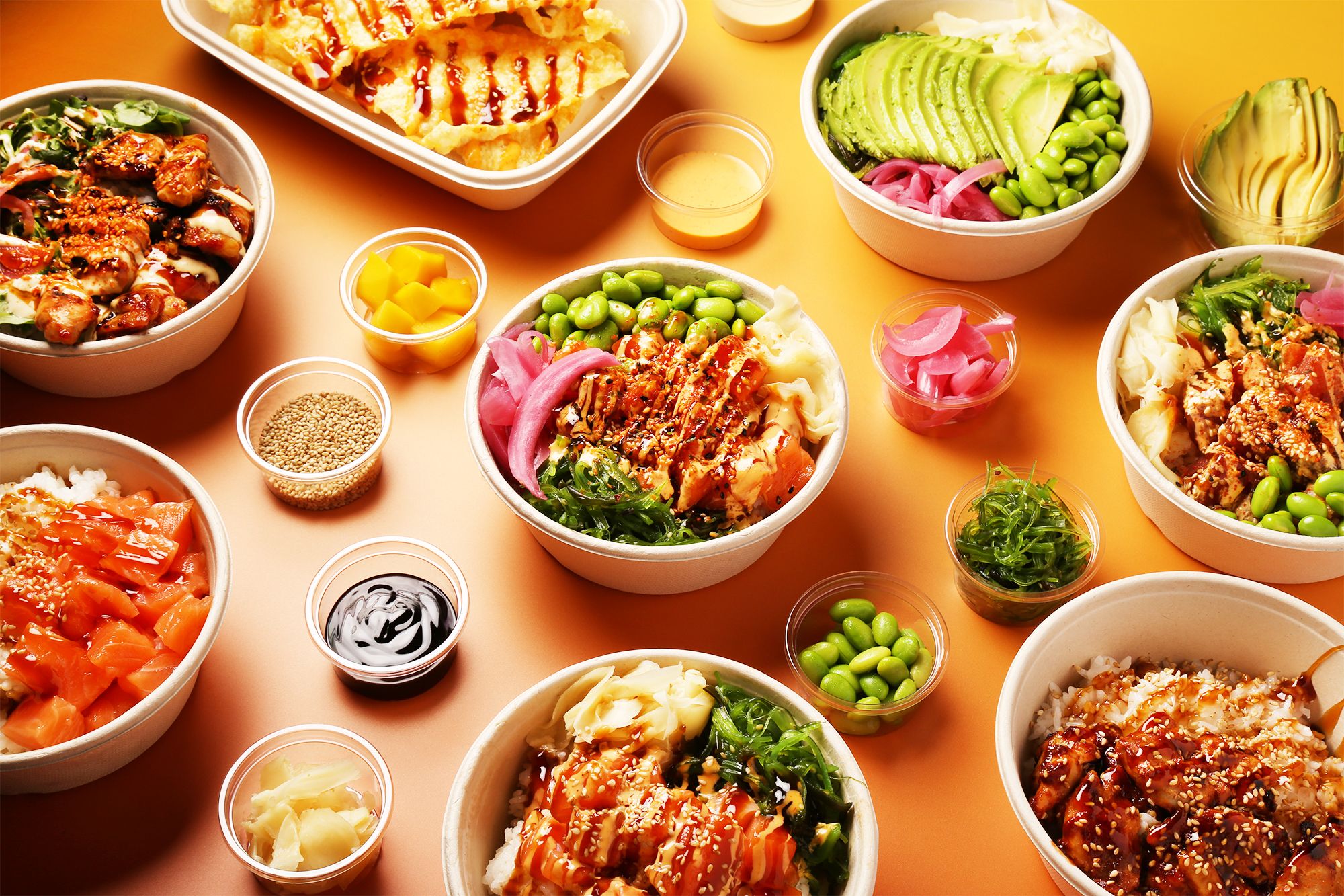 Bowls, poke nachos og små skåler med tilbehør dekket opp på oransje bakgrunn, sett ovenfra.